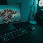 High angle of computer monitor with keyboard and mouse placed on table near CPU in dark workplace